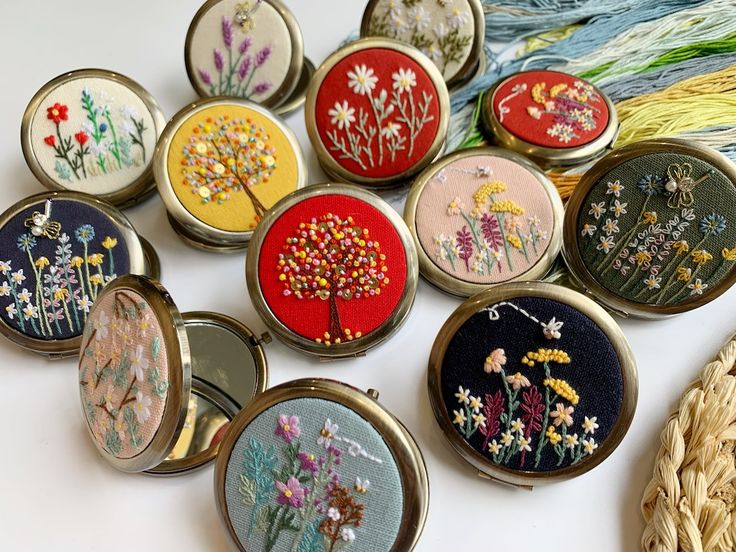 a collection of embroidered flowers and plants in small compact cases on a white table top