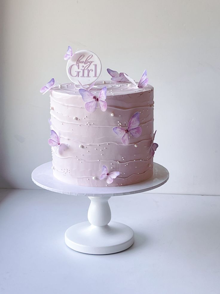 a pink cake with purple butterflies on it sitting on top of a white pedestal in front of a wall