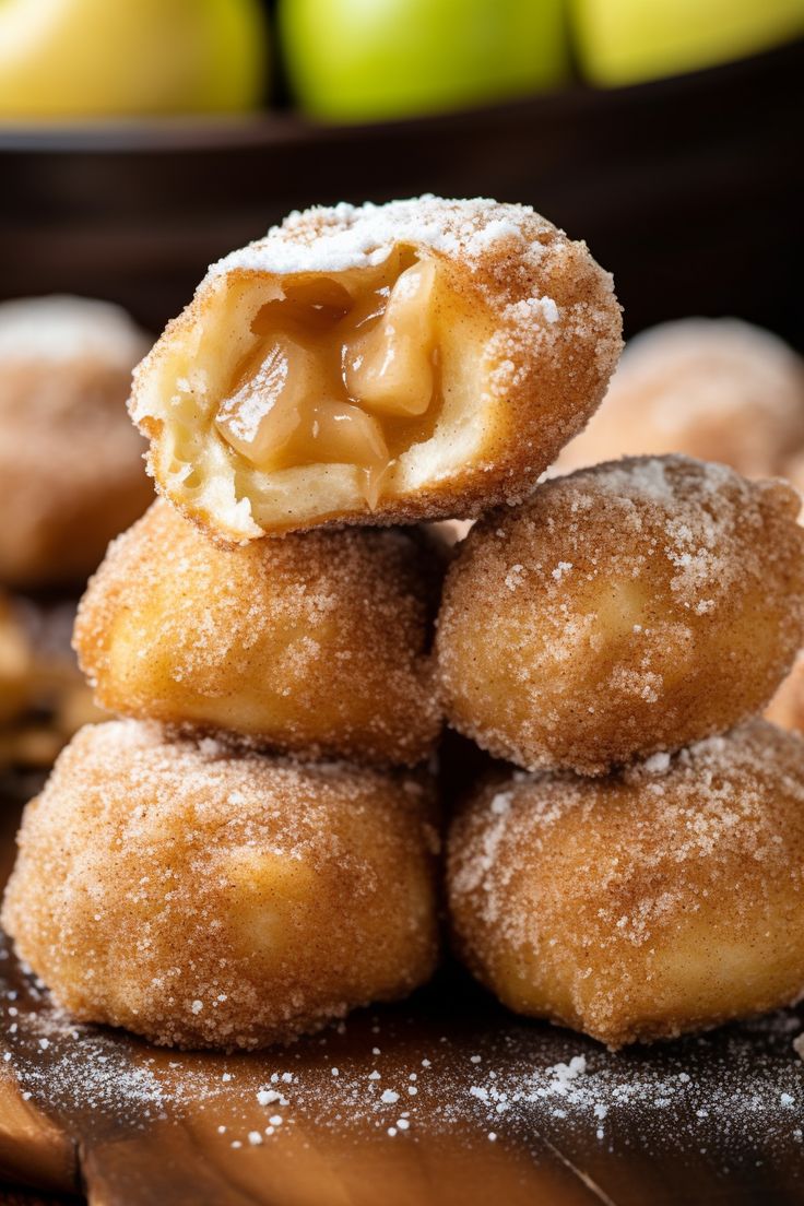 a pile of doughnuts sitting on top of each other with apples in the background