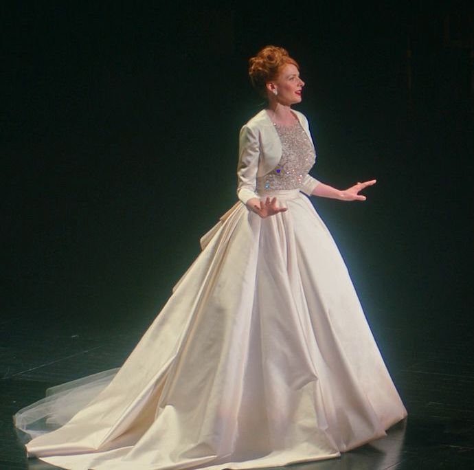 a woman in a white dress on stage with her hands out to the side,