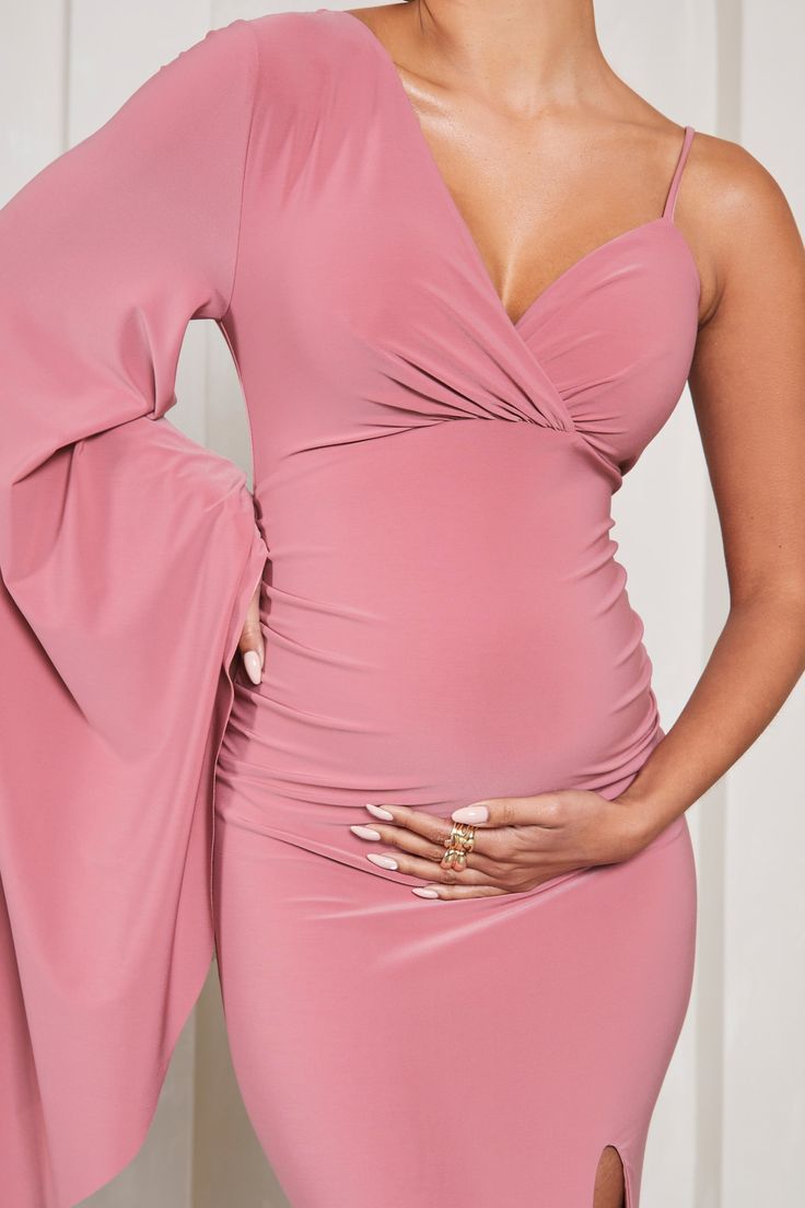 Perfect for baby showers. weddings and everything in between. Rhea is a formal wardrobe must-have. Crafted in a soft pink shade of our signature stretch jersey. this v-neck maternity maxi dress was designed with your comfort at the forefront. Characterised by a singular cape sleeve. Rhea concludes with subtle bump ruching and a high-leg split. Features - Premium stretch jersey- V neckline- Single cape sleeve- Adjustable cami strap- Invisible zip closure - Bump ruching - High-leg split- Maxi leng Pink Stretch Maternity Dress For Spring, Feminine Pink V-neck Maternity Dress, Fitted Pink Maternity Dress In Feminine Style, Feminine Fitted Pink Maternity Dress, Fitted Pink Feminine Maternity Dress, Pink Fitted Maternity Dress, Pink Stretch Maternity Dress, Pink Ruched Maternity Dress, Pink Ruched Dress For Wedding Guest