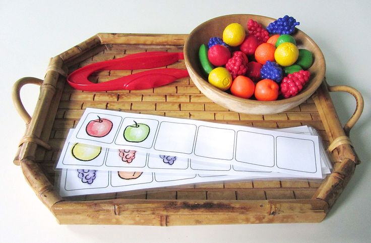 a wooden tray holding a bowl of fruit next to a matching game board with scissors