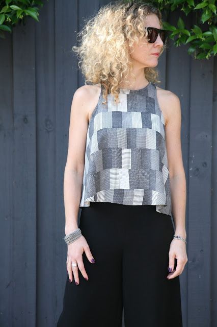 a woman standing in front of a fence wearing black pants and a cropped top