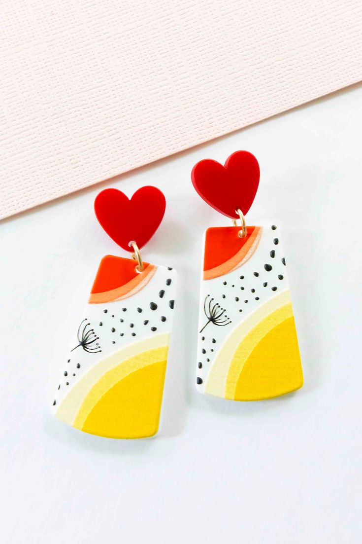 two heart shaped earrings on top of a white table next to a piece of paper