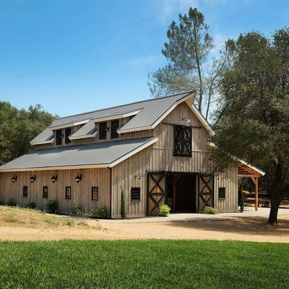 an old barn with a metal roof in the middle of a dirt field next to trees