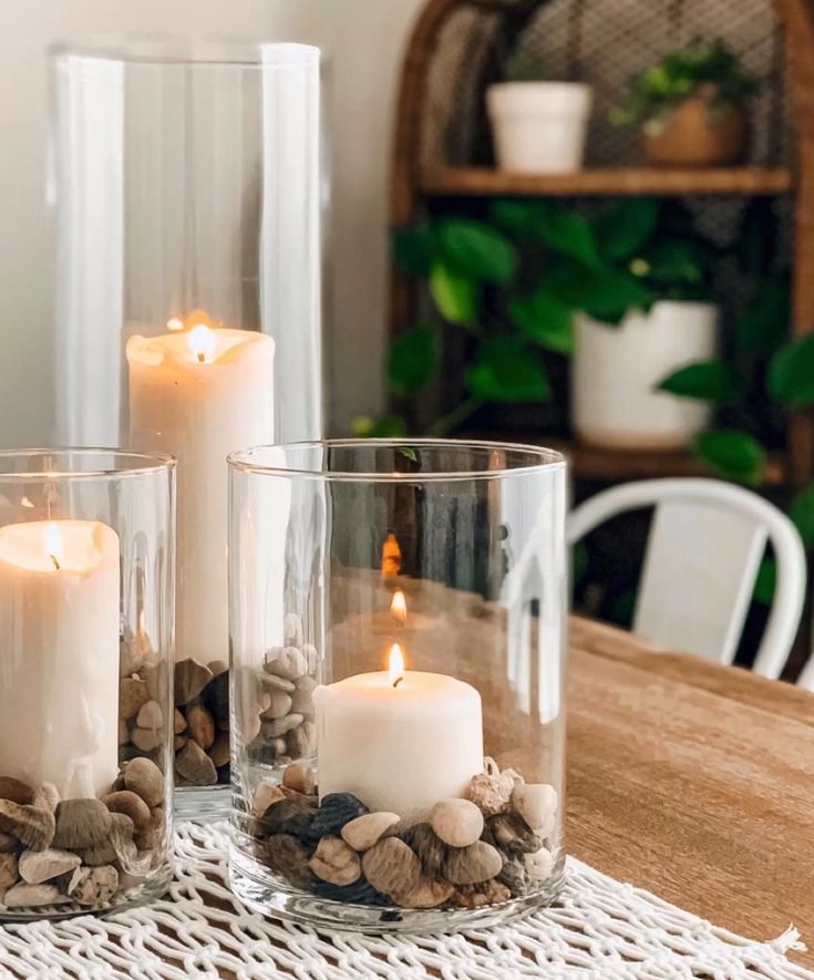 three clear glass vases filled with rocks and lit candles on top of a wooden table