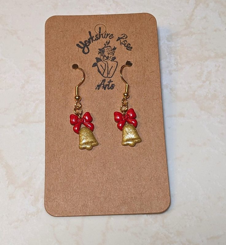 Introducing our elegant Golden Bells Earrings - a breathtaking fusion of sophistication and festive charm. Crafted from polymer clay, these earrings exude the opulent beauty of sparkling gold bells adorned with vibrant red ribbons, creating a statement accessory that embodies the spirit of the season. Each bell is meticulously detailed to capture the richness and shimmer of real gold, ensuring you radiate elegance at every holiday gathering. The festive red ribbons delicately tied on top add a t Shimmer N Shine, Holiday Wardrobe, Holiday Gathering, Red Ribbon, Vibrant Red, Real Gold, Jewelry Earrings Dangle, Timeless Fashion, Etsy Earrings