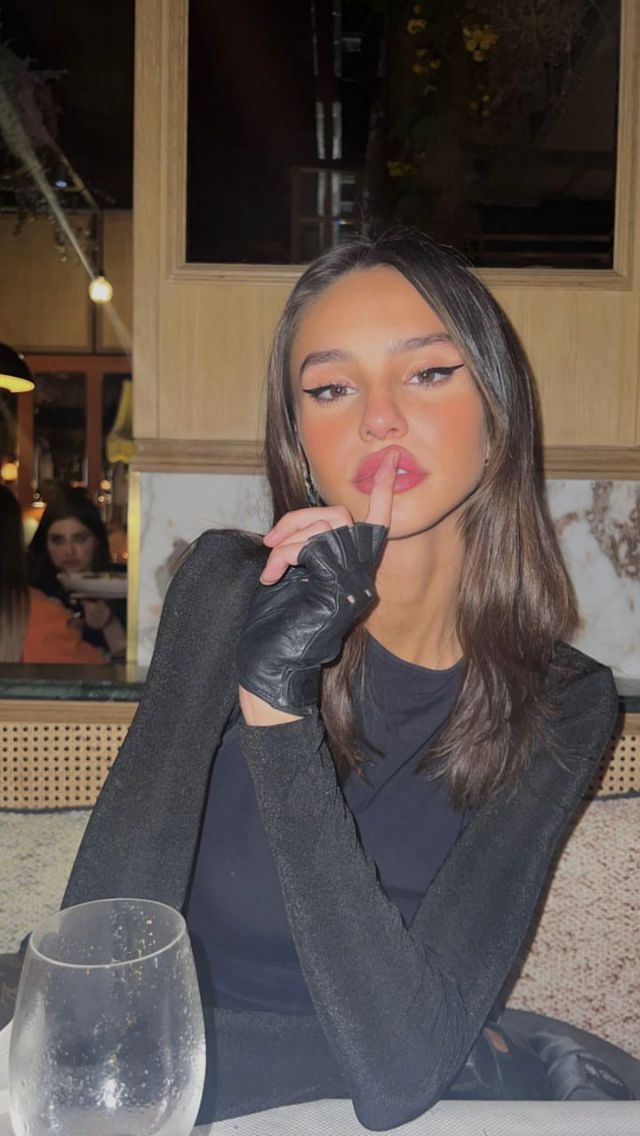 a woman sitting at a table with a wine glass in front of her and finger on her lips