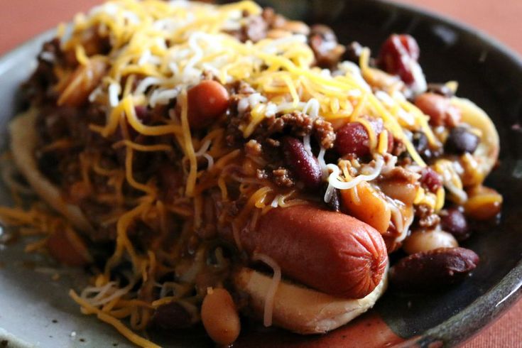 a hot dog covered in chili, beans and cheese on top of a black plate