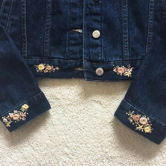 a denim jacket with embroidered flowers on the front and back, sitting on a white carpet