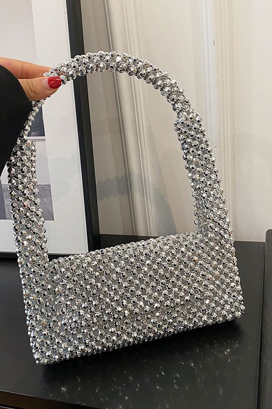 a hand holding a silver purse on top of a black table next to a mirror