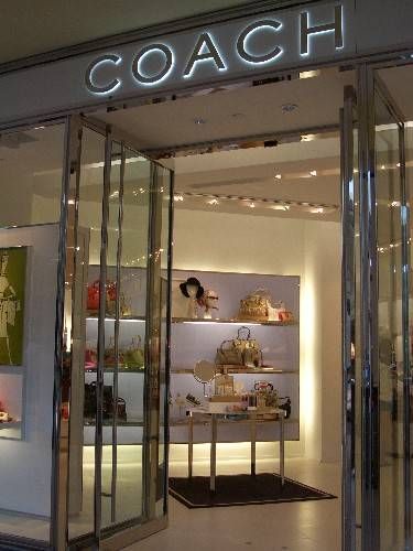 a coach store front with its lights on and the door open to show it's products