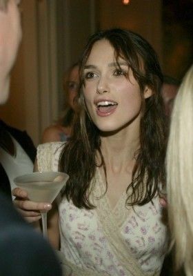 a woman holding a martini glass in her right hand and talking to another person at a party