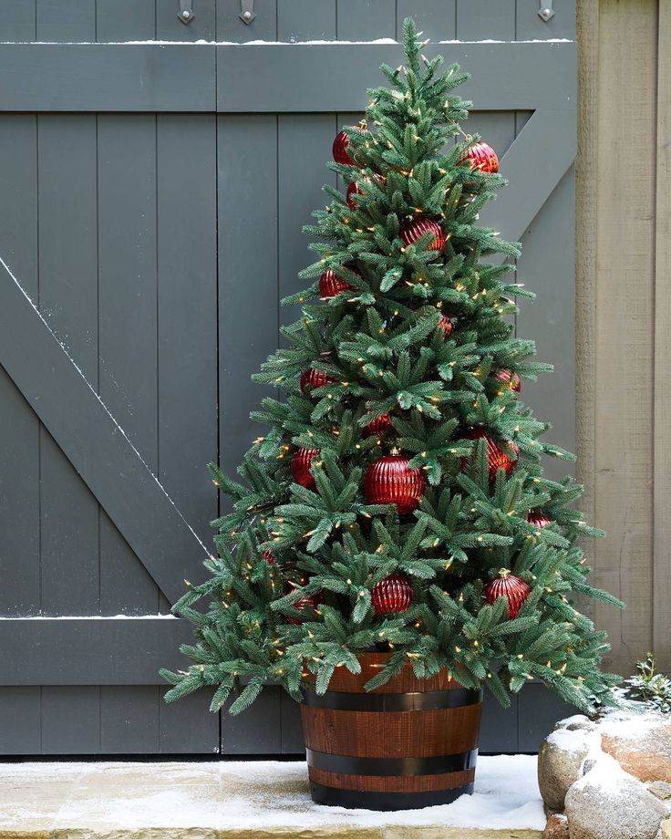 a small christmas tree with red ornaments in a wooden barrel next to a barn door