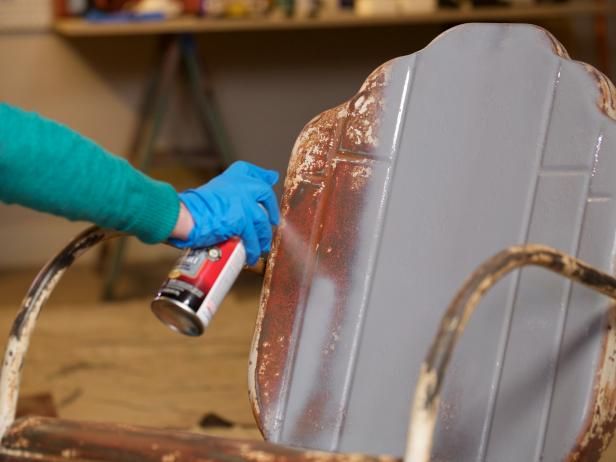 a person in blue gloves spray painting an old metal chair with rusted paint on it