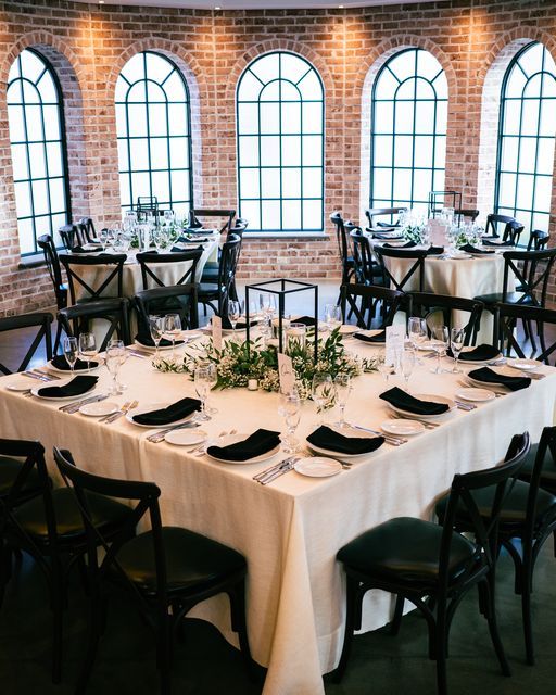 a table set up with place settings and black chairs in front of three large windows