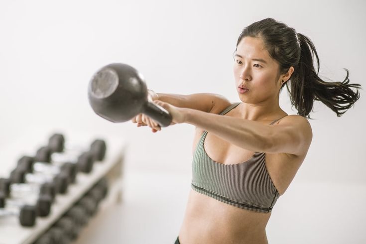 a woman holding a kettle in front of a row of dumbbells