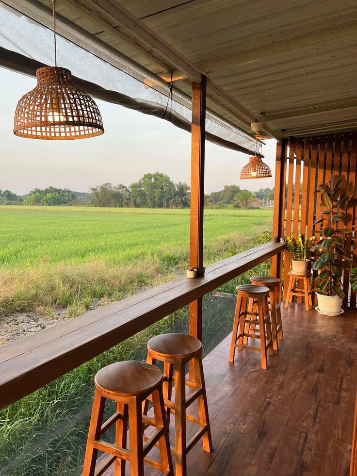 a porch with wooden stools and lights on the ceiling, overlooking an open field