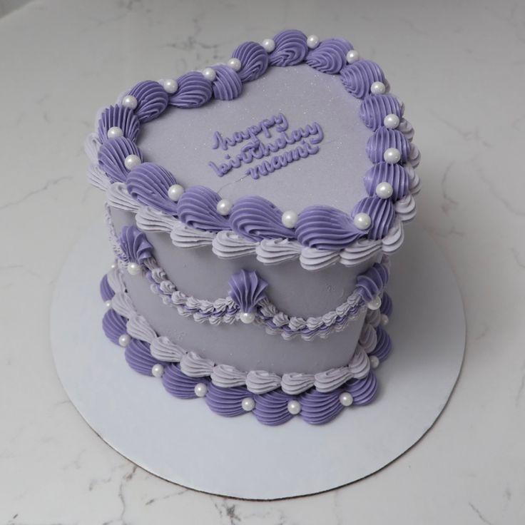 a heart shaped birthday cake with purple icing and pearls on the top, sitting on a white plate