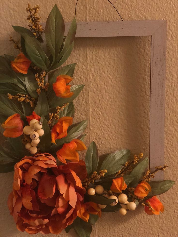 an orange flower is hanging on the wall in front of a frame with leaves and berries