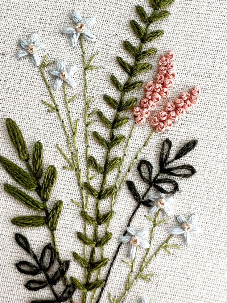 some flowers and leaves are on a white fabric background with stitching in the middle