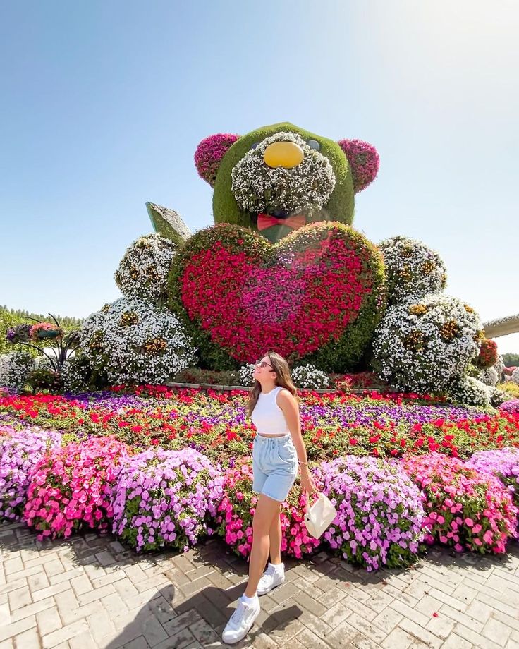 a woman standing in front of a large teddy bear made out of flowers and plants