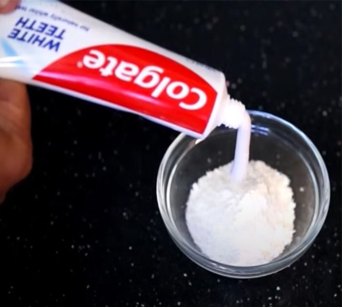 a person is holding a tube of toothpaste in a small glass bowl on a counter