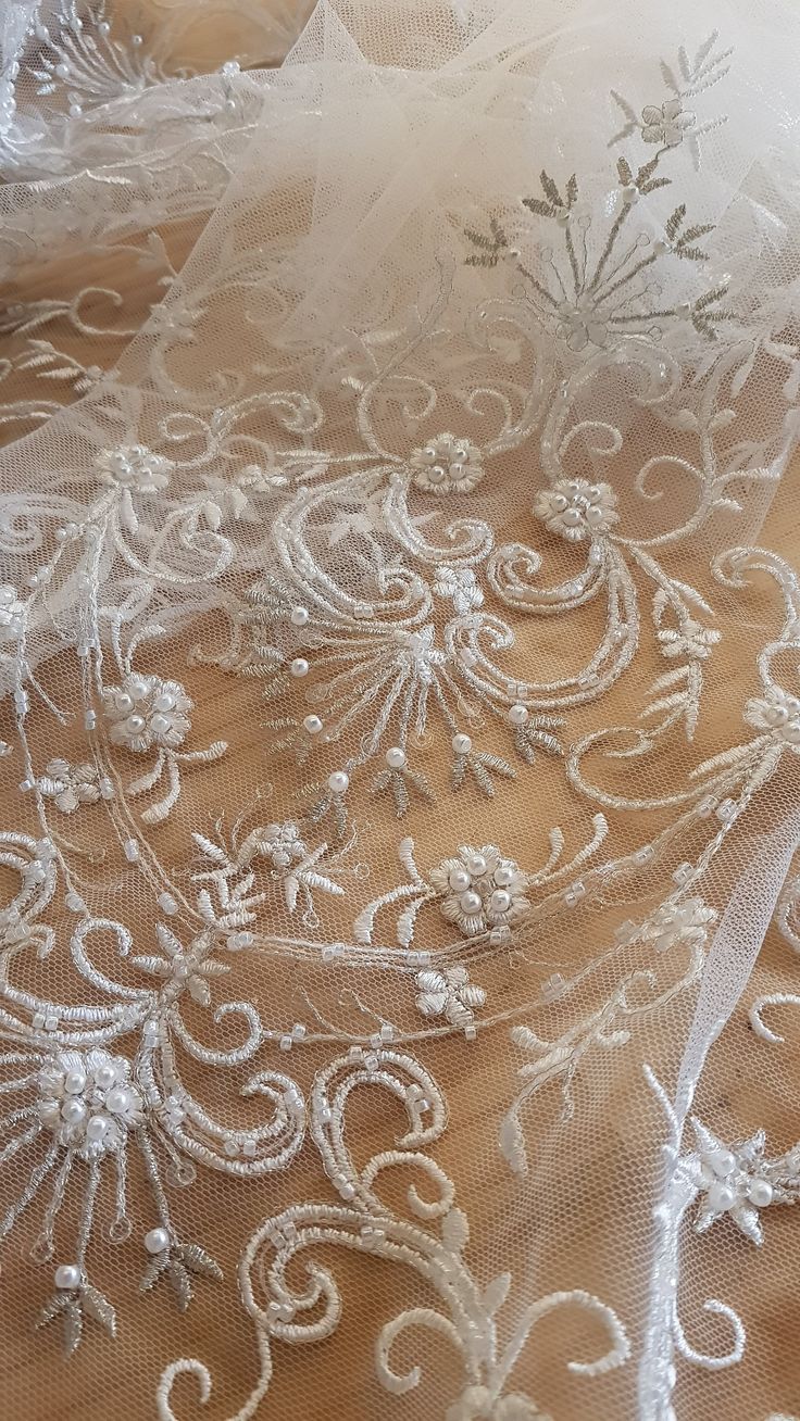 closeup of white embroidered fabric with flowers and vines on the bottom, along with sheer tulle