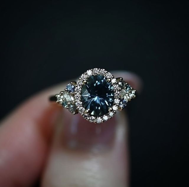 a close up of a person's hand holding a ring with a blue and white diamond