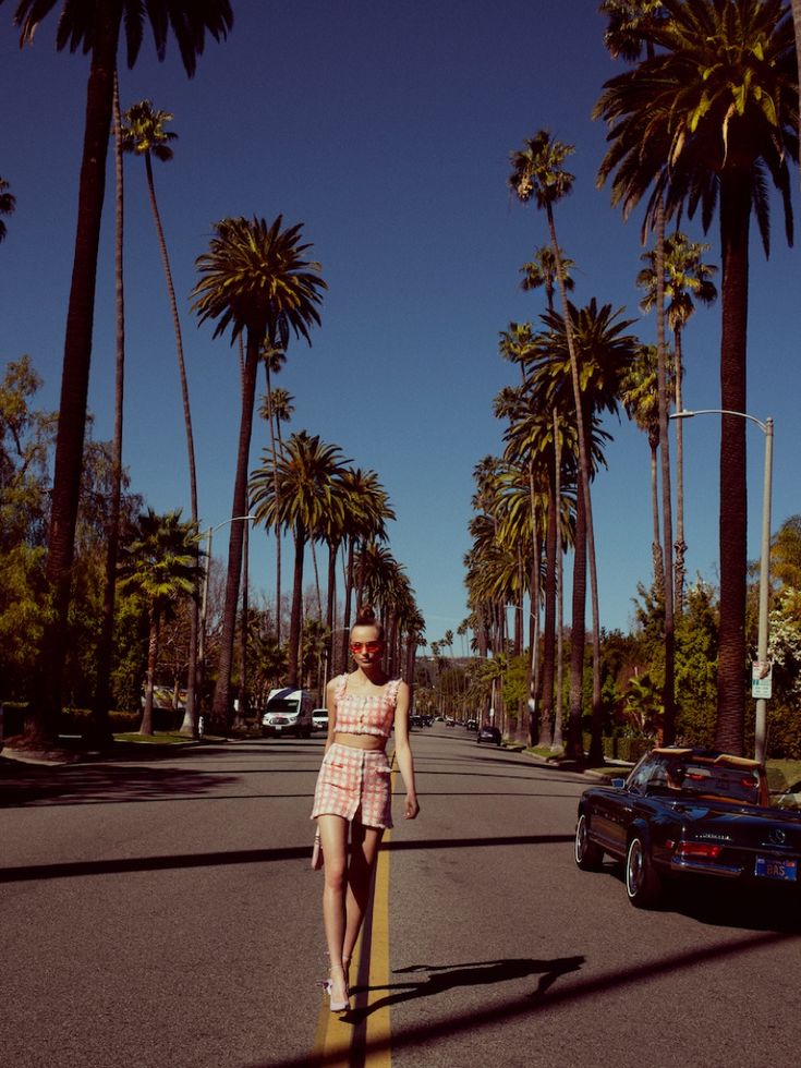 a woman walking down the street in front of palm trees