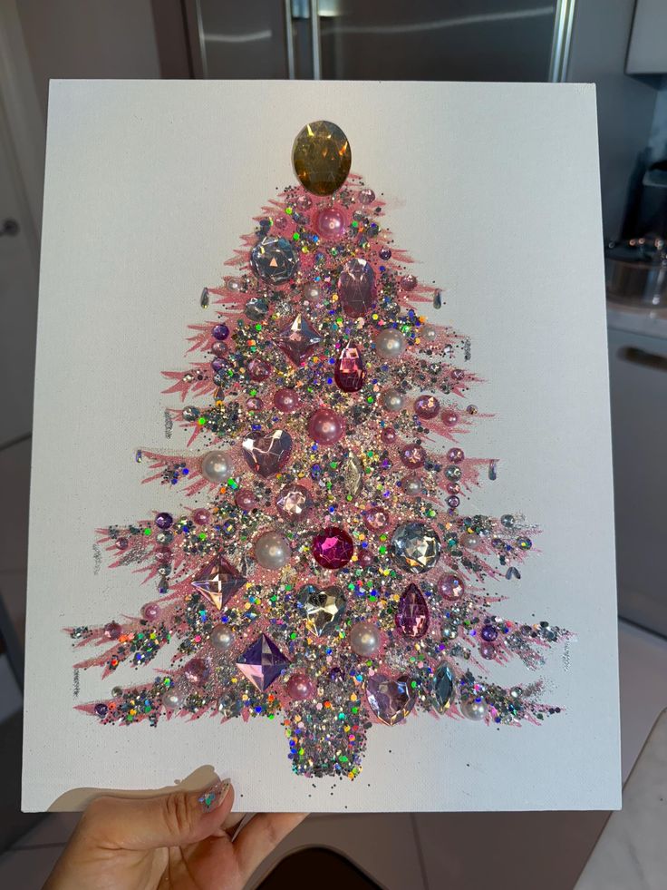 a person holding up a card with a christmas tree made out of jewels on it