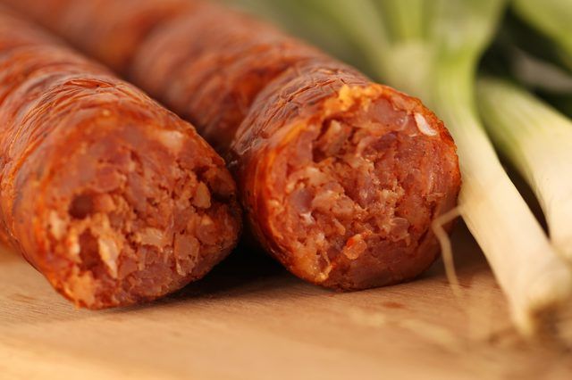 two sausages sitting on top of a cutting board next to onions and celery