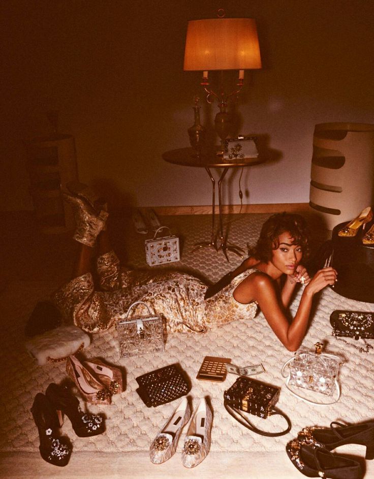 a woman laying on top of a bed surrounded by purses and shoes in a room