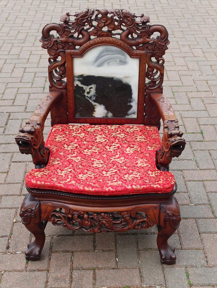 an ornate wooden chair with a red cushion on the ground and a mirror in the back