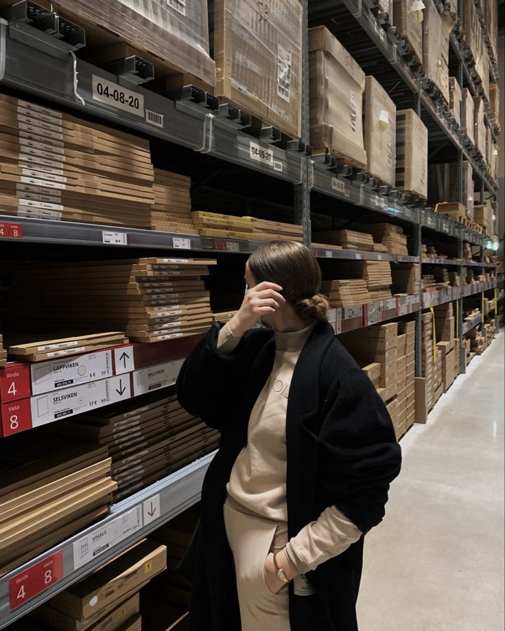 a woman is talking on her cell phone in a warehouse with shelves full of boxes