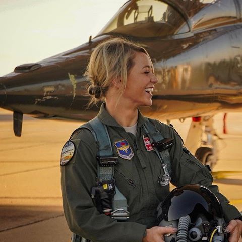 a woman in an air force pilot's uniform standing next to a fighter jet