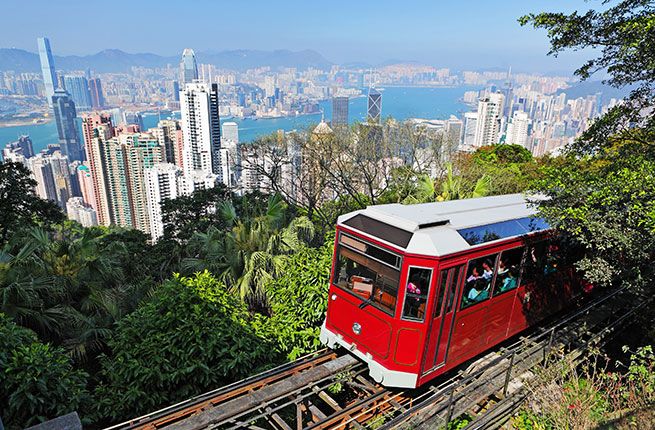 a red and white train traveling through a lush green forest next to the city skyline