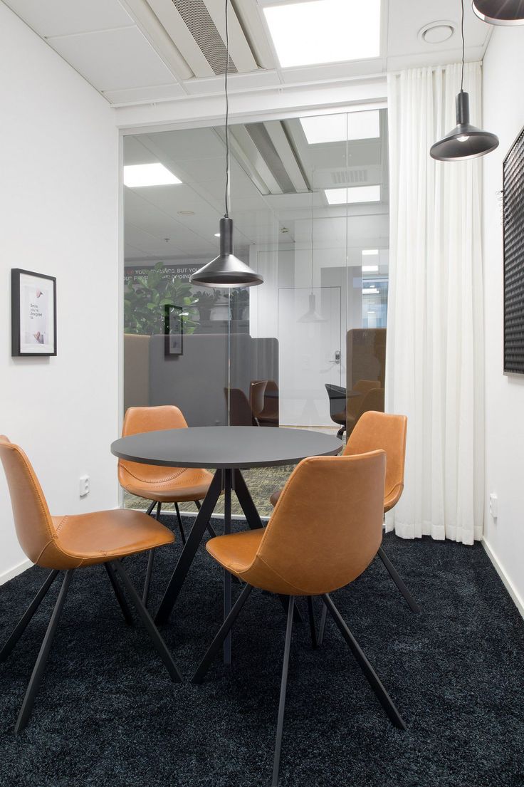 an office with black carpet, orange chairs and a round table in front of a window