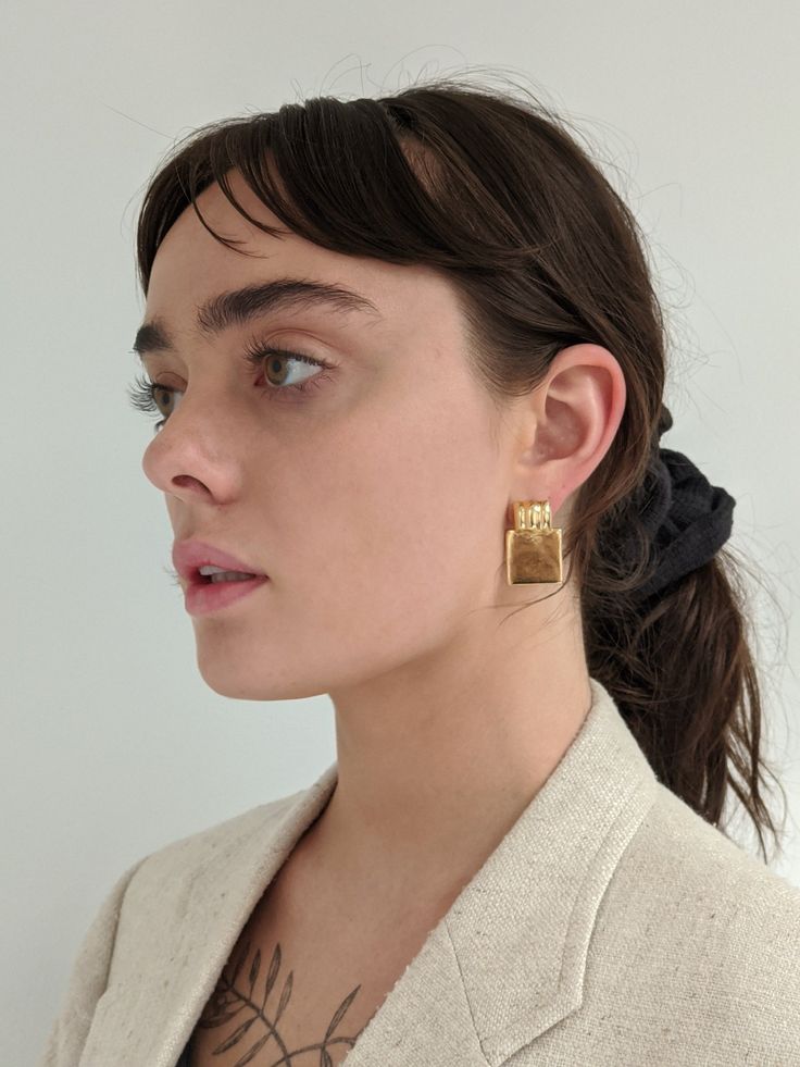 a woman wearing gold earrings and a white blazer