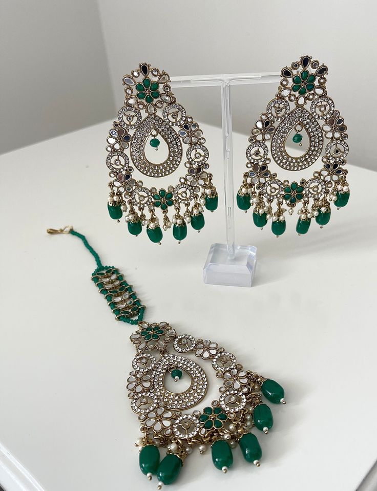 A gold and silver style set which comes with earrings and a tikka.   This set comes with dangling beads along the bottom that are available in silver or green  Follow our Instagram page @sakavano_jewellery for all our latest offers.  ---------------------------------------------- Please DM or email for any enquires.  Please also note we do not offer any refunds or exchanges.  ------------------------------------------------ Green Kundan Tikka For Eid, Festive Heavy Green Tikka, Elegant Green Tikka With Tilla Detail, Elegant Green Tikka For Festive Occasions, Elegant Green Tikka For Festive Season, Bollywood Style Green Tikka For Diwali, Green Bollywood Style Tikka For Diwali, Green Bollywood Tikka For Diwali, Heavy Green Tikka For Diwali