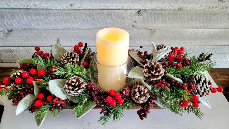 a candle is sitting on a table with holly and pine cones