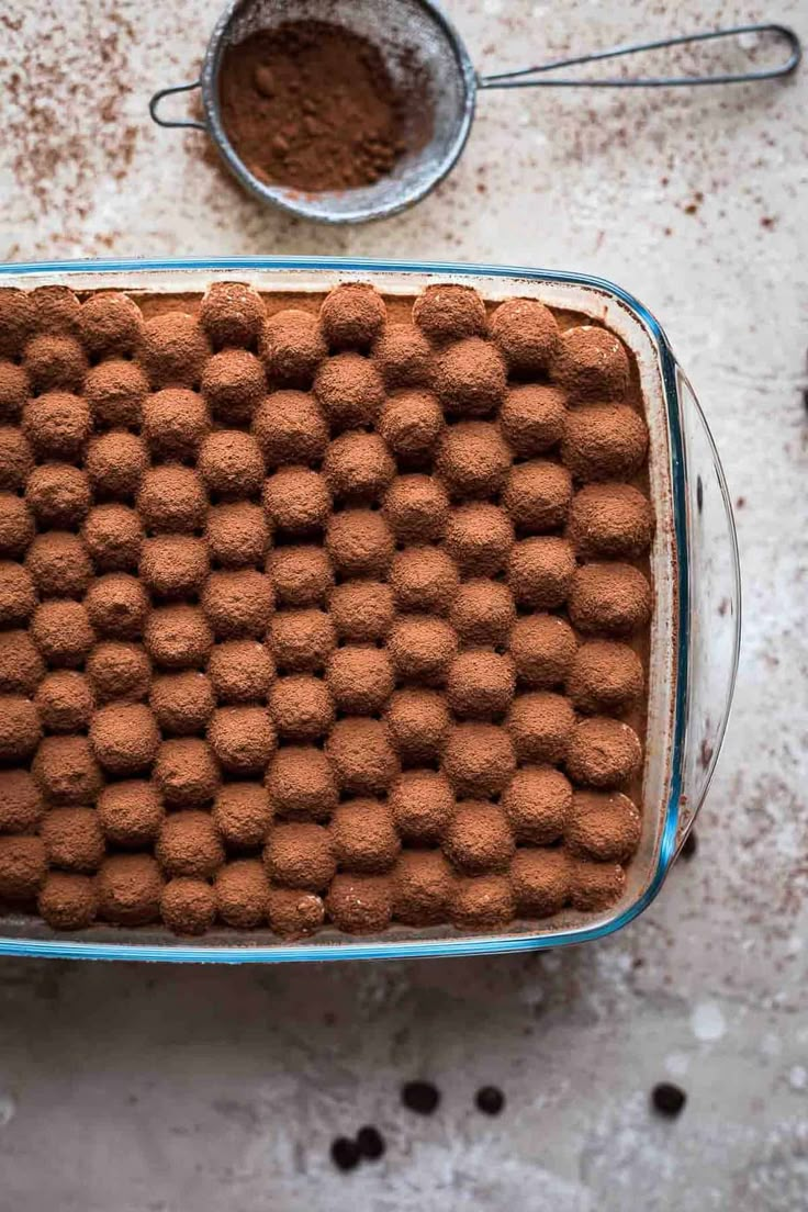 a baking dish filled with chocolate balls next to measuring spoons and cocoa powder on a table