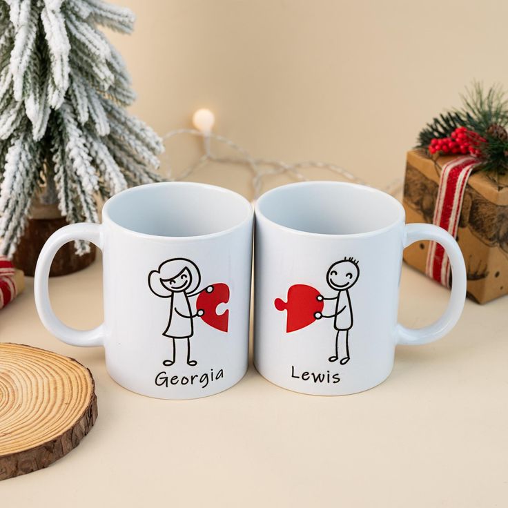 two coffee mugs sitting next to each other on top of a table in front of a christmas tree