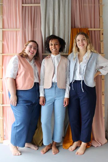 three women standing next to each other in front of a window with pink drapes