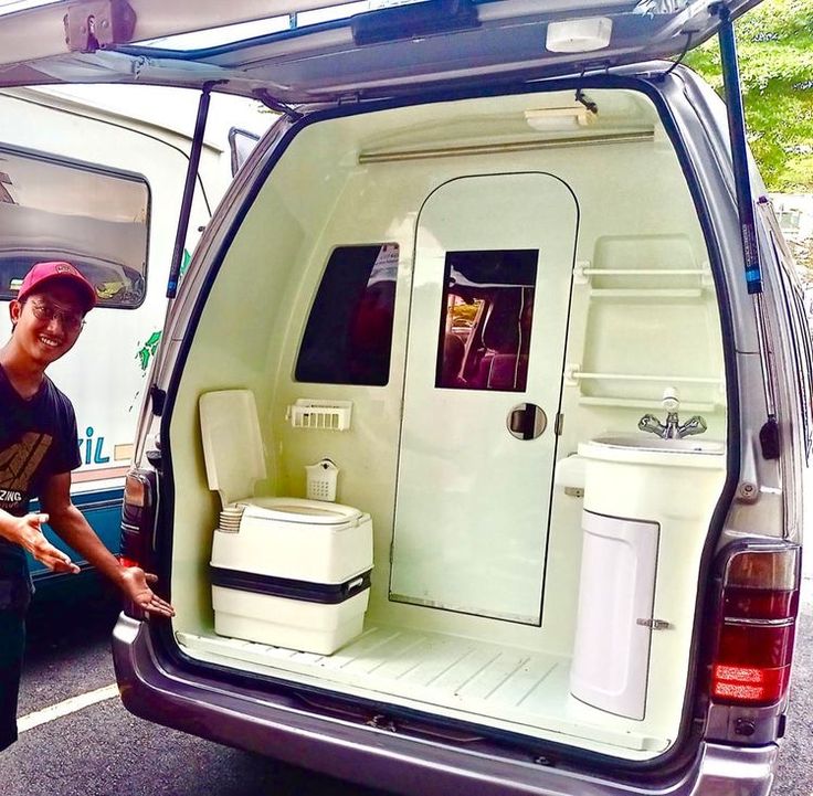 a man standing next to a van with its door open and toilet in the back