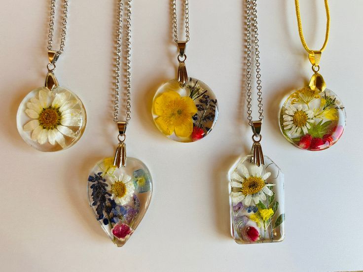 four glass pendants with flowers on them hanging from chain necklaces against a white background