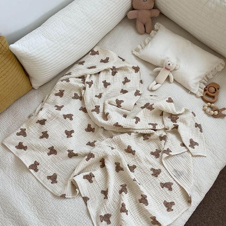 a teddy bear laying on top of a white bed next to pillows and stuffed animals