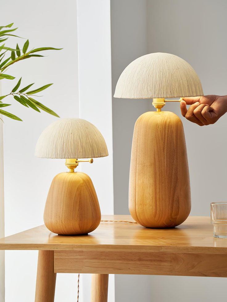 two wooden lamps sitting on top of a table next to a vase with a plant in it