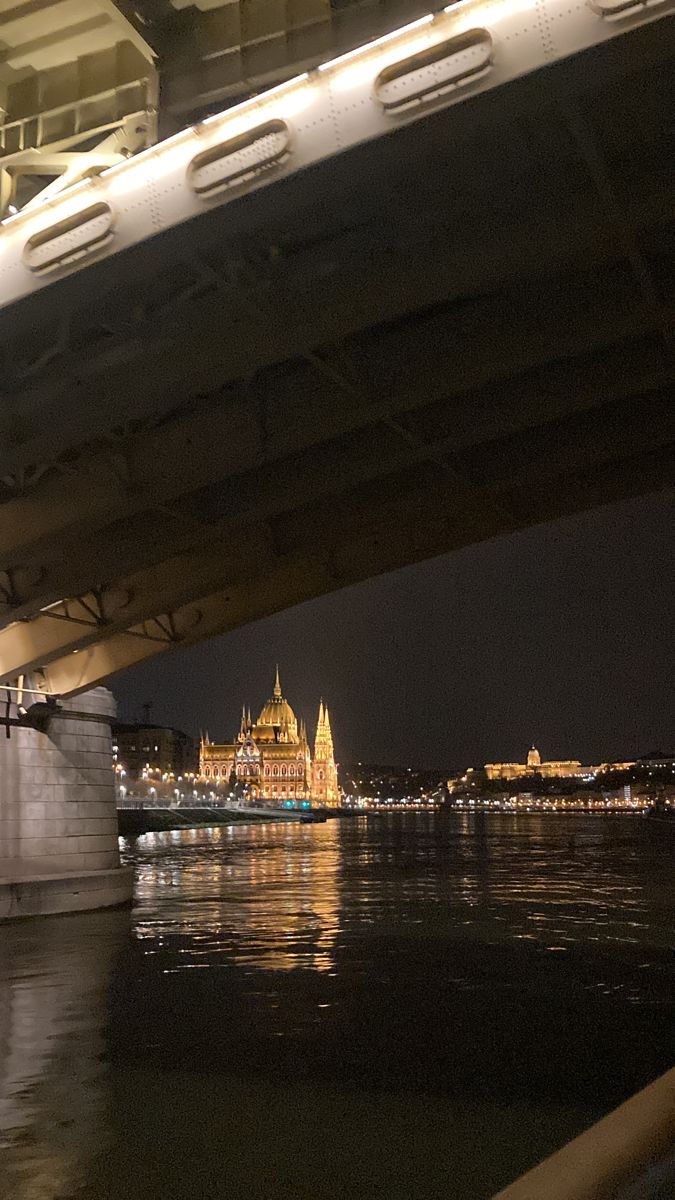 a bridge over the water at night with lights on it's sides and buildings in the background