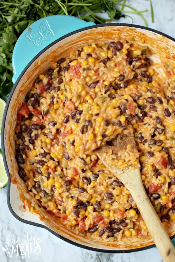 a pot filled with rice and beans next to a wooden spoon on top of a table